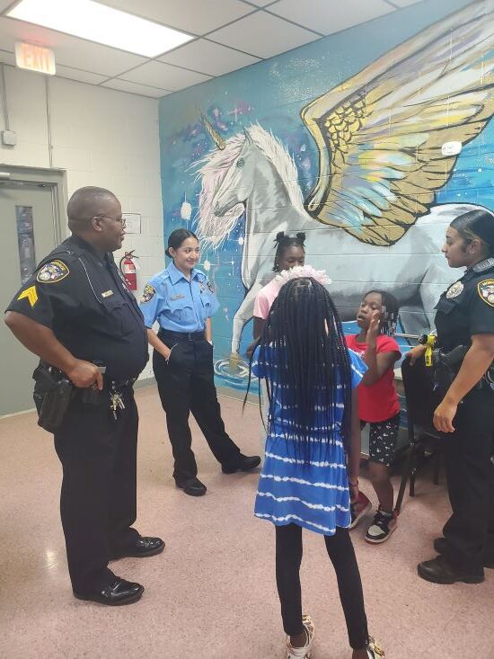 Officers and children standing in front of a winged horse mural. 