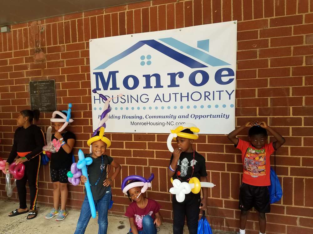 kids with balloon toys in front of Monroe housing authority sign