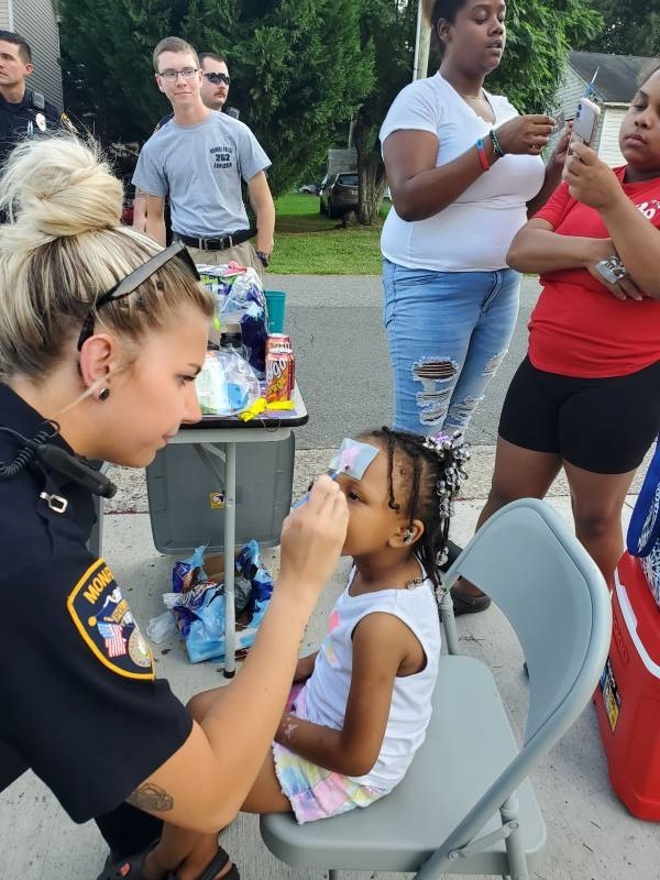 A young woman police officer painting on the face of a young girl.