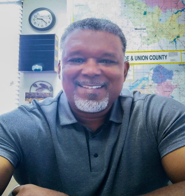 Calvin Davis smiles a bright smile while sitting at a desk. 