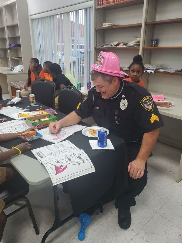 Police officer wearing a fireman's hat coloring with children. 