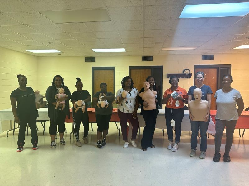CPR class members standing and holding training dummies along with their teacher. 