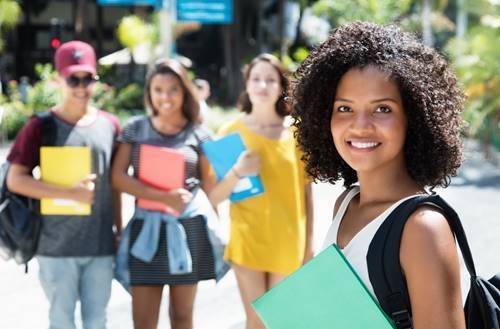 BJM Beyond Scholarship. Girl outside holding a binder. Other students in the background.