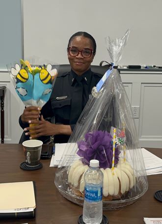 Lieutenant Hold smiles and holds a bouquet of flowers while seated behind a Bundt cake.