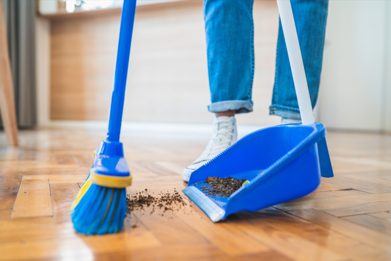 Person standing with a broom and dust pan sweeping up dirt. 